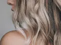 Kobieta z falowanymi, blond włosami ozdobionymi nowoczesnymi pasemkami, ukazana od ramienia.
