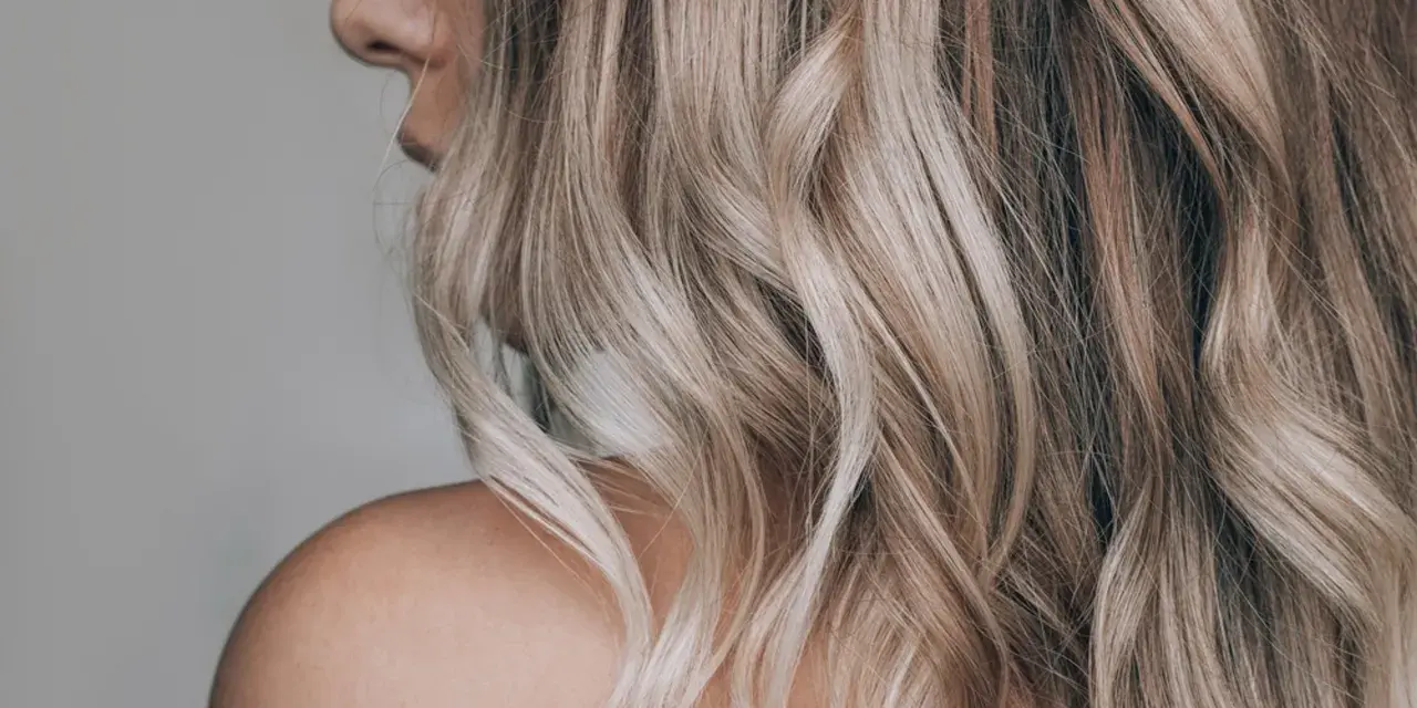 Kobieta z falowanymi, blond włosami ozdobionymi nowoczesnymi pasemkami, ukazana od ramienia.
