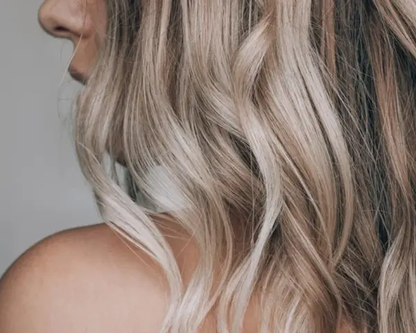 Kobieta z falowanymi, blond włosami ozdobionymi nowoczesnymi pasemkami, ukazana od ramienia.