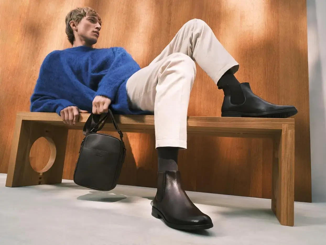 Eleganckie, skórzane botki to idealne buty do chinosów. Mężczyzna w niebieskim swetrze prezentuje stylową stylizację.